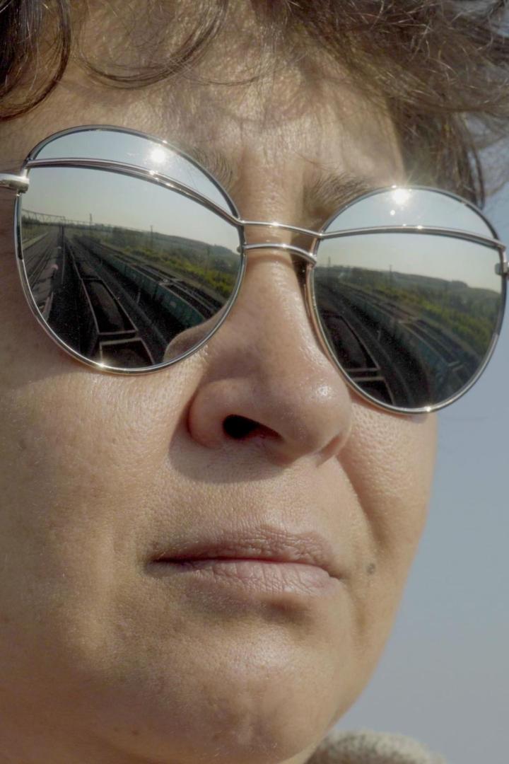 Das Spiegelbild einer Zugstrecke in den Brillengläsern einer Frau.