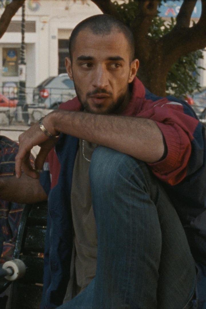 Ein Mann sitzt auf einer Bank im Freien und raucht eine Zigarette.