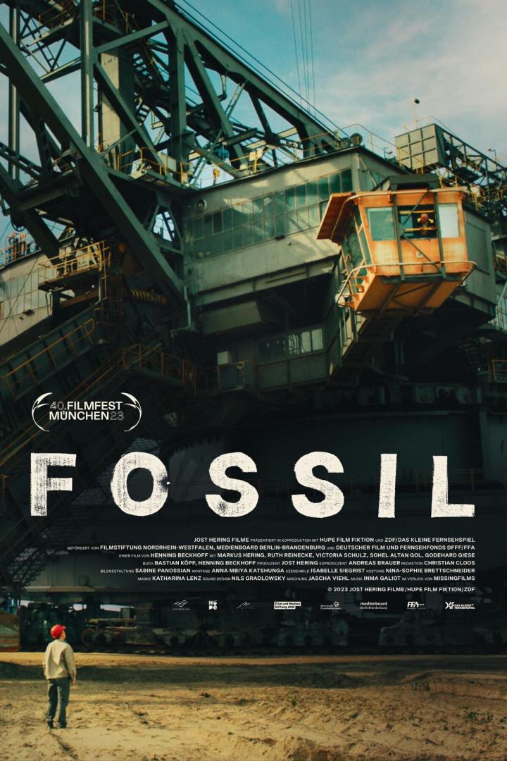 Ein Mann steht vor einem riesigen Schaufelradbagger auf dem Filmplakat zu „Fossil“.