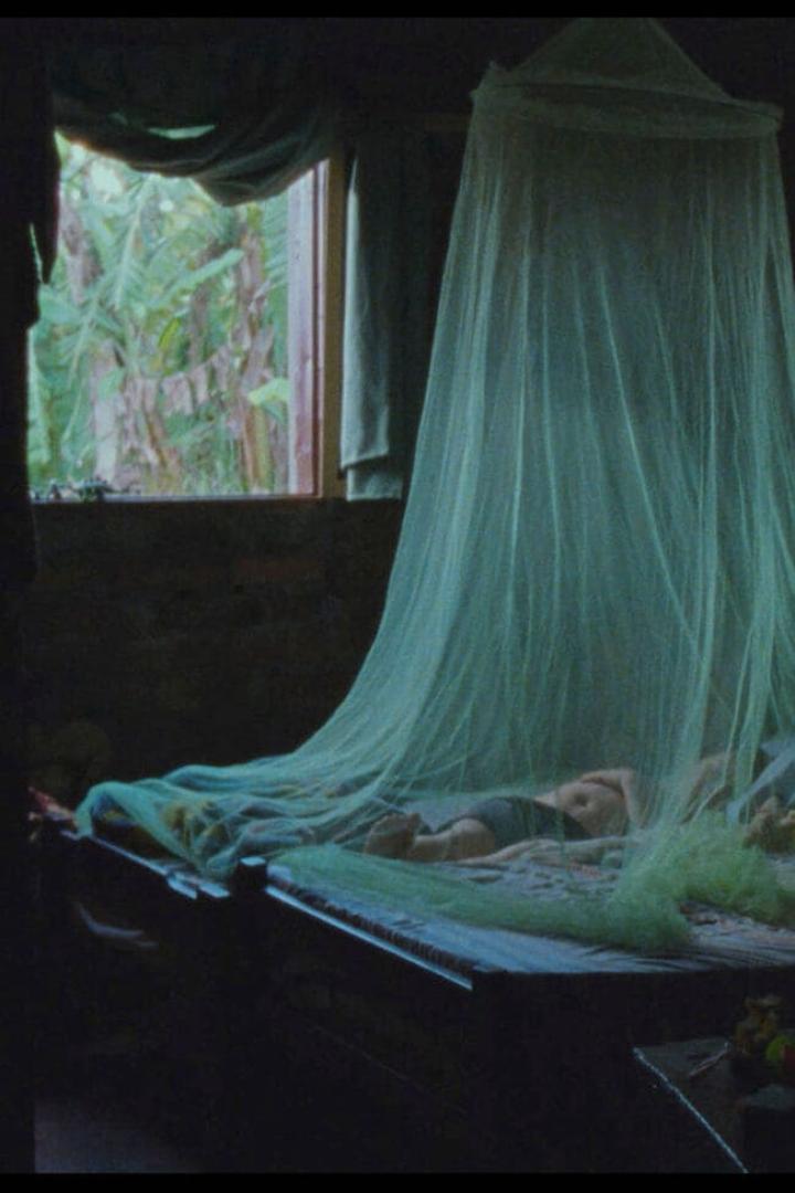 Ein Kind schläft unter einem Moskitonetz in einem dunklen Raum.