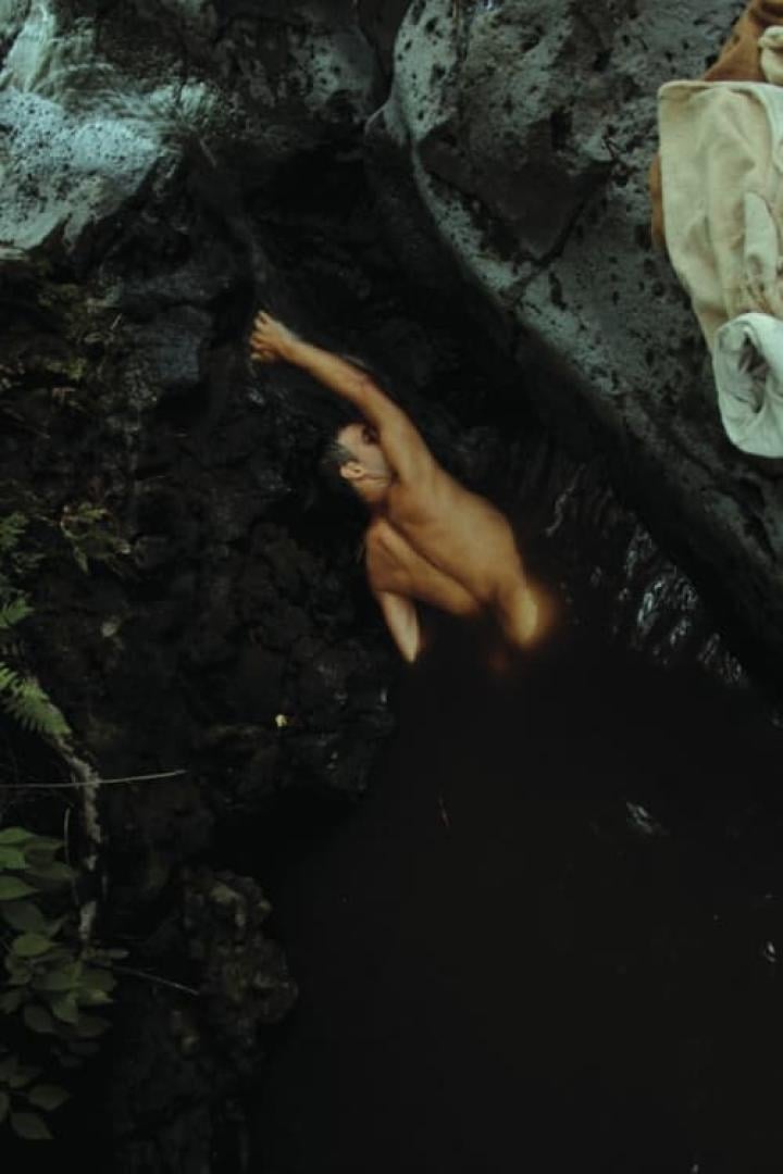 Ein Mann badet in einem dunklen Felsentümpel.