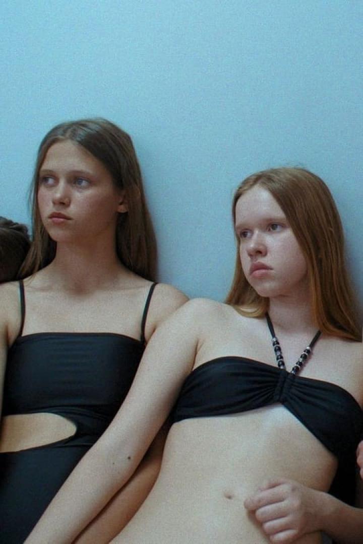 Zwei junge Frauen in Badebekleidung posieren vor einer hellblauen Wand.