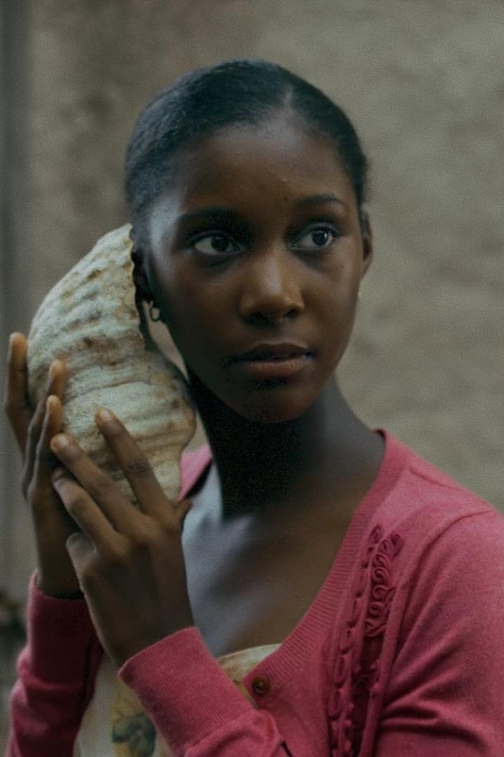 Eine junge Frau hält eine große Muschel an ihr Ohr.