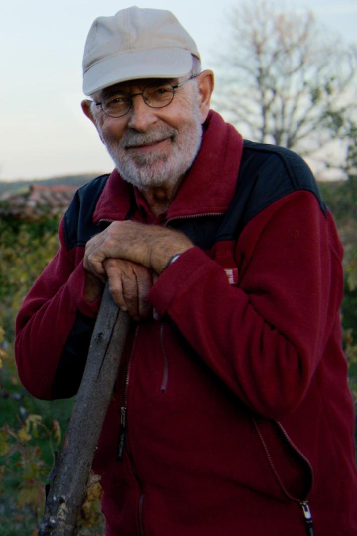 Ein älterer Mann mit Brille und Mütze lächelt und stützt sich auf einen Stock.