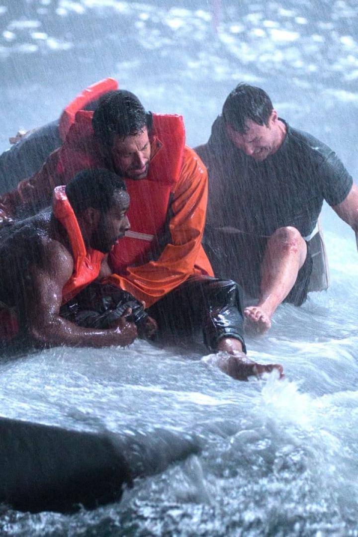 Drei Männer in Rettungswesten kämpfen im stürmischen Wasser.