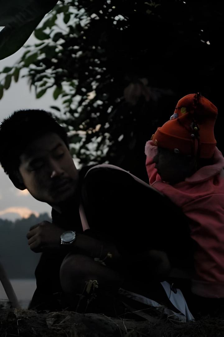 Ein Mann hält ein Kind mit Mütze im Arm, vermutlich im Freien.