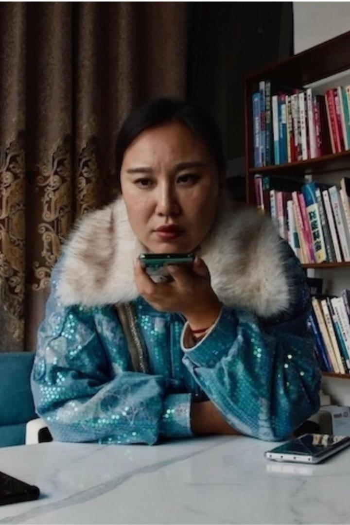 Eine Frau in einer glitzernden Jacke spricht in ihr Smartphone.