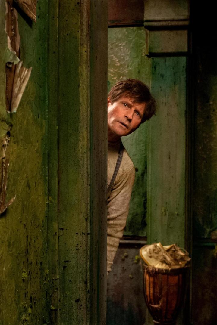 Ein Mann späht hinter einer grünen, abgenutzten Tür hervor.