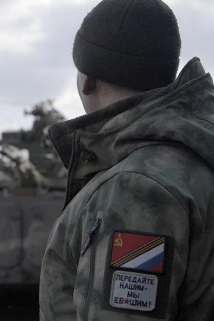 Ein Soldat mit Mütze und Tarnjacke, auf der ein Abzeichen mit russischer Flagge und Sowjetstern zu sehen ist.