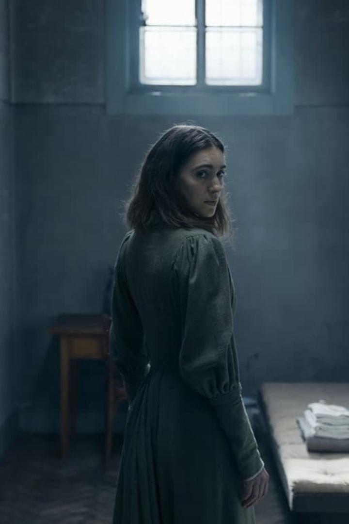 Eine Frau in einem grünen Kleid blickt in einem düsteren Raum über ihre Schulter.