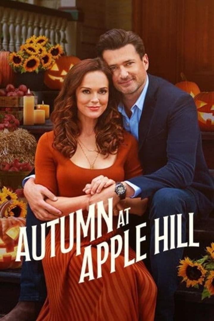 Ein Mann und eine Frau umarmen sich vor dem Hintergrund von Kürbissen und Herbstdekorationen für den Film „Autumn at Apple Hill“.