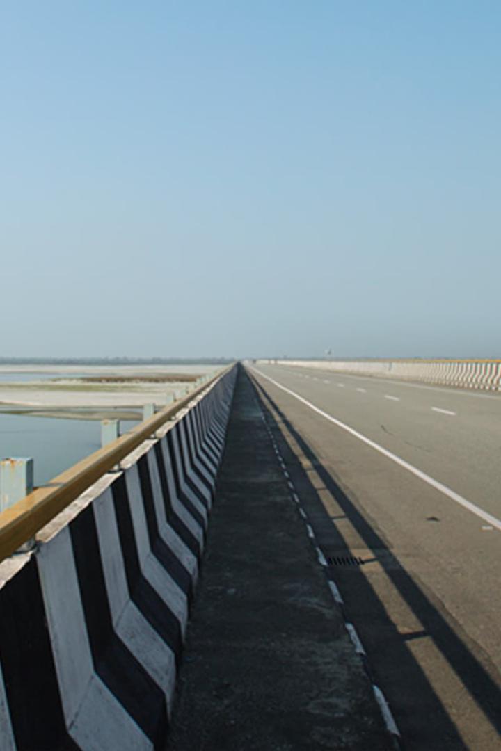 Eine lange Brücke erstreckt sich über eine weite Ebene unter einem hellen Himmel.