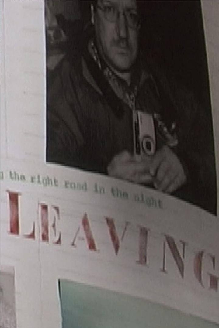 Ein Mann mit Brille und Schnurrbart hält eine Kamera in den Händen, unter dem Wort „Leaving“.