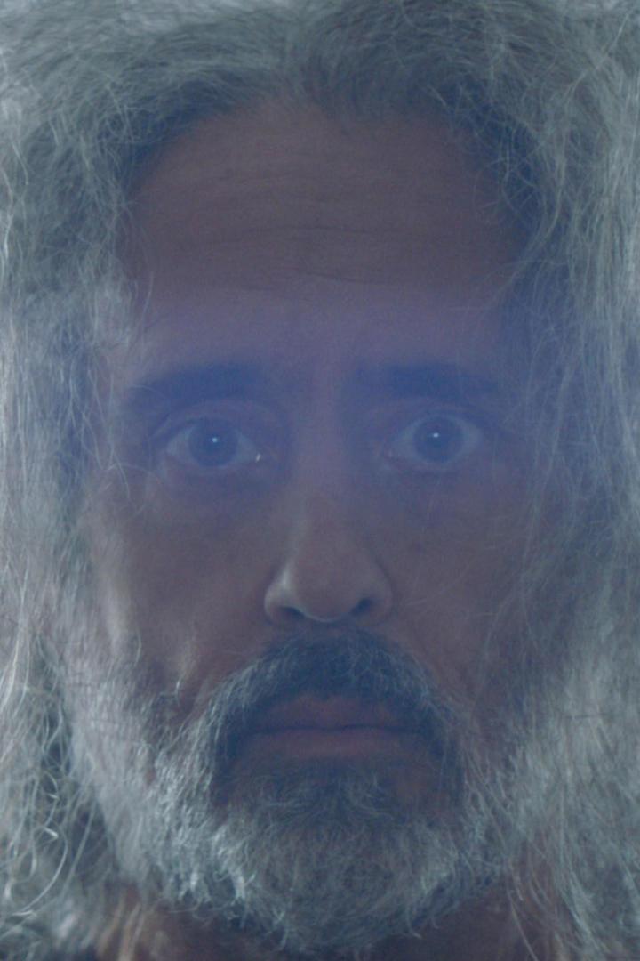 Ein Mann mit Bart und langen, grauen Haaren blickt in die Kamera.