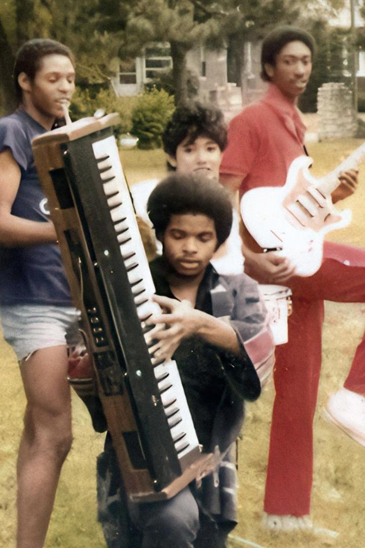 Eine Gruppe junger Männer posiert mit Musikinstrumenten, darunter ein Keyboard und eine Gitarre.