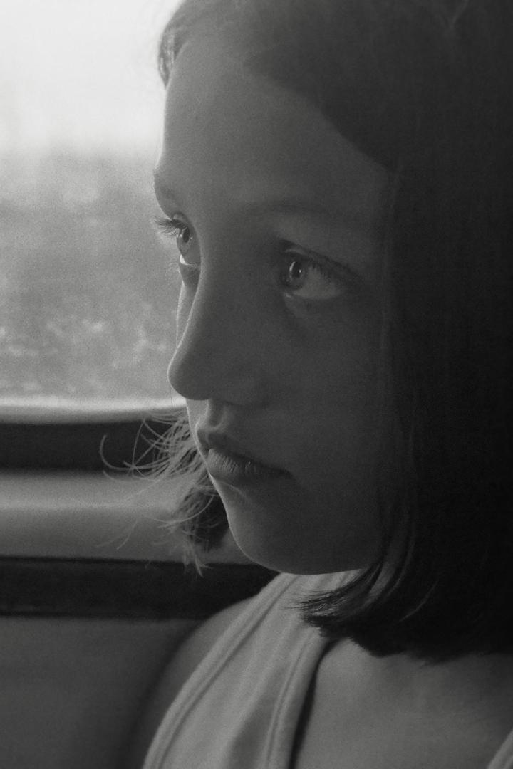 Ein Schwarzweißporträt eines jungen Mädchens, das aus dem Fenster schaut.