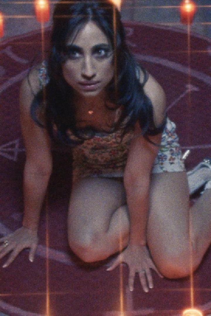 Eine Frau kniet auf einem roten Teppich mit einem aufgemalten Pentagramm.