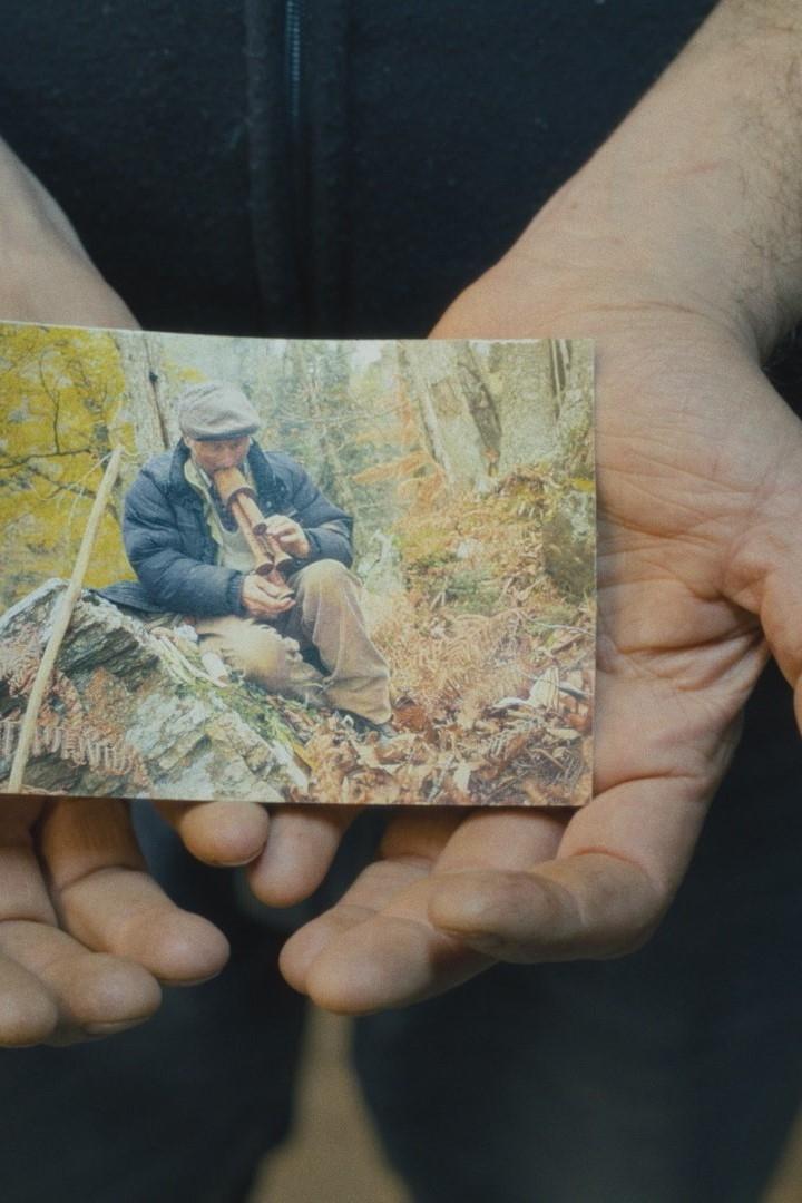 Eine Person hält ein Foto von einem Mann, der in einem Wald sitzt und eine Pfeife raucht.