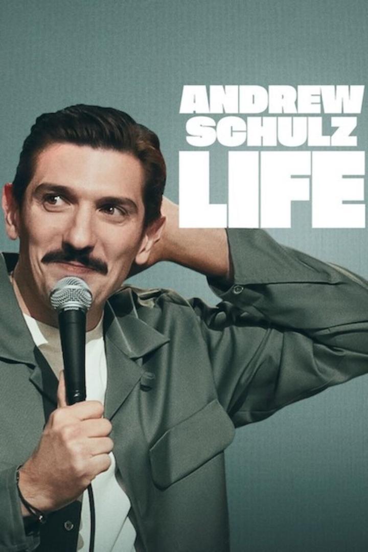 Der Comedian Andrew Schulz mit Mikrofon vor dem Cover seines Programms „Life“.