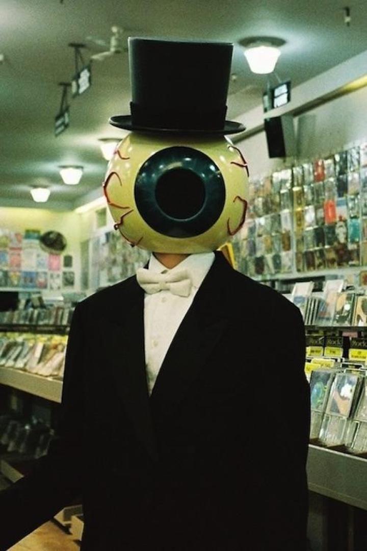 Eine Person mit einem Augapfel-Kopf und Zylinder in einem Geschäft.