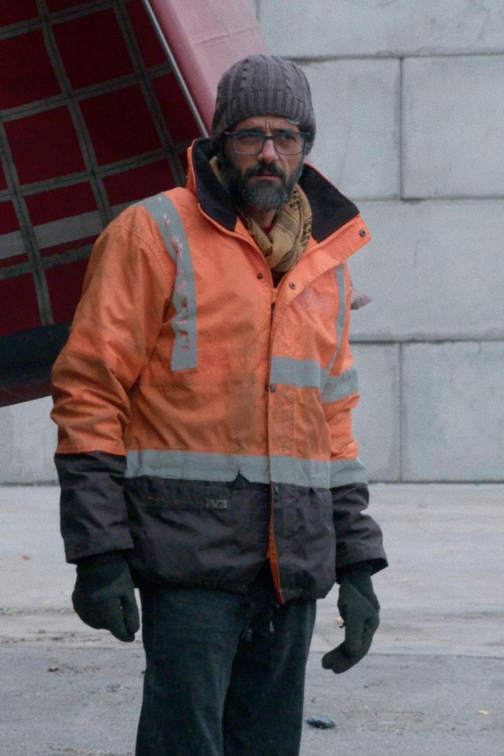 Ein Mann mit Brille und Mütze trägt eine orangefarbene Arbeitsjacke.