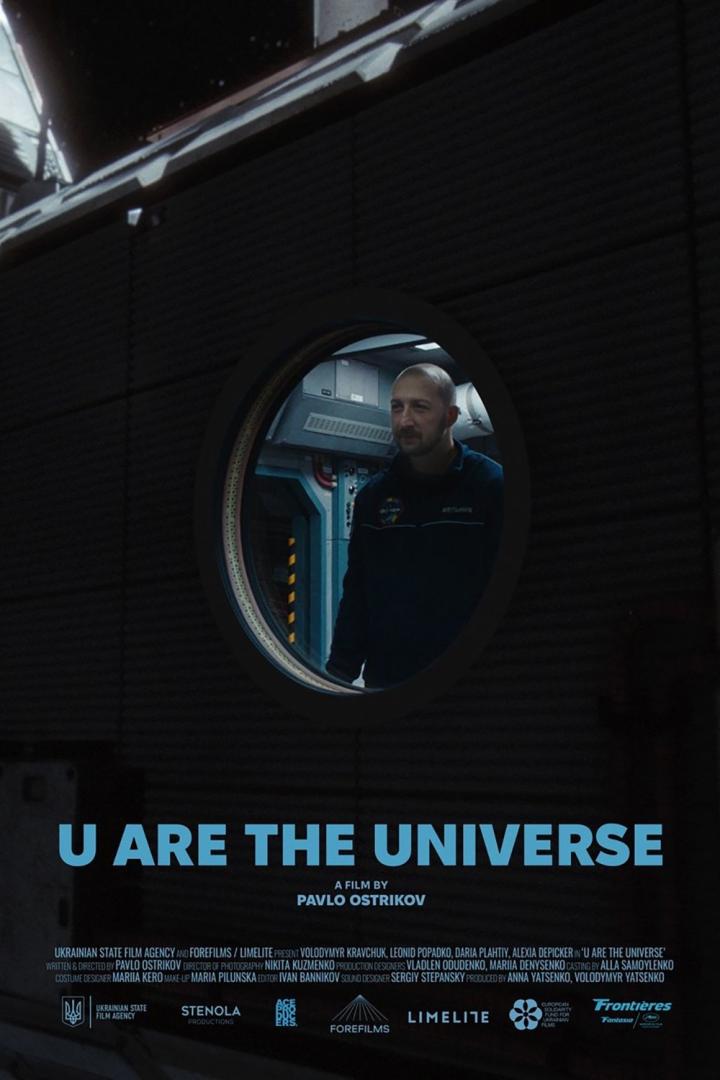Ein Mann in Astronautenkleidung schaut aus einem Bullauge in dem Film „U Are the Universe“.