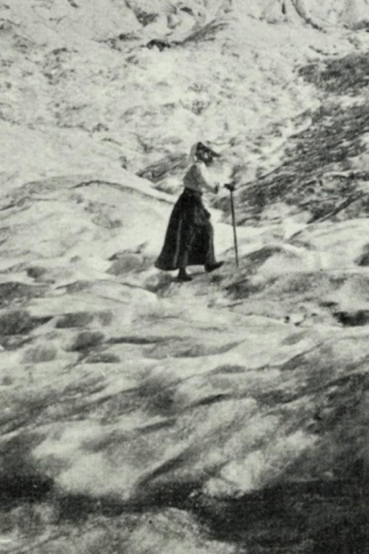Eine Frau mit Stock wandert in einer Berglandschaft.