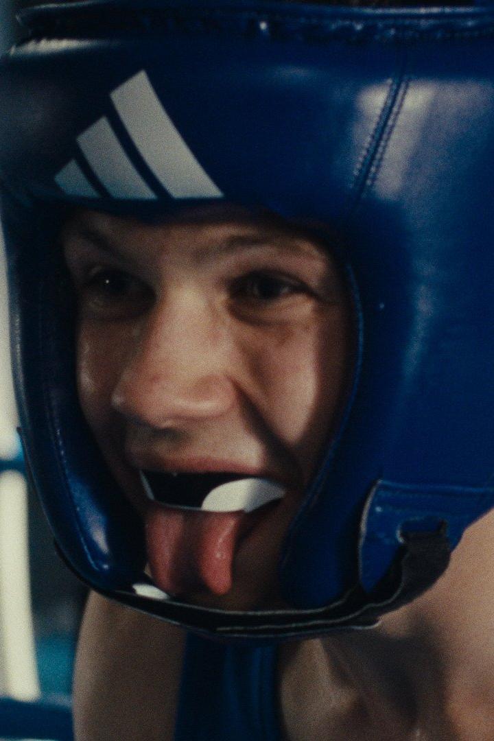 Ein Boxer mit blauem Kopfschutz und Mundschutz streckt die Zunge heraus.