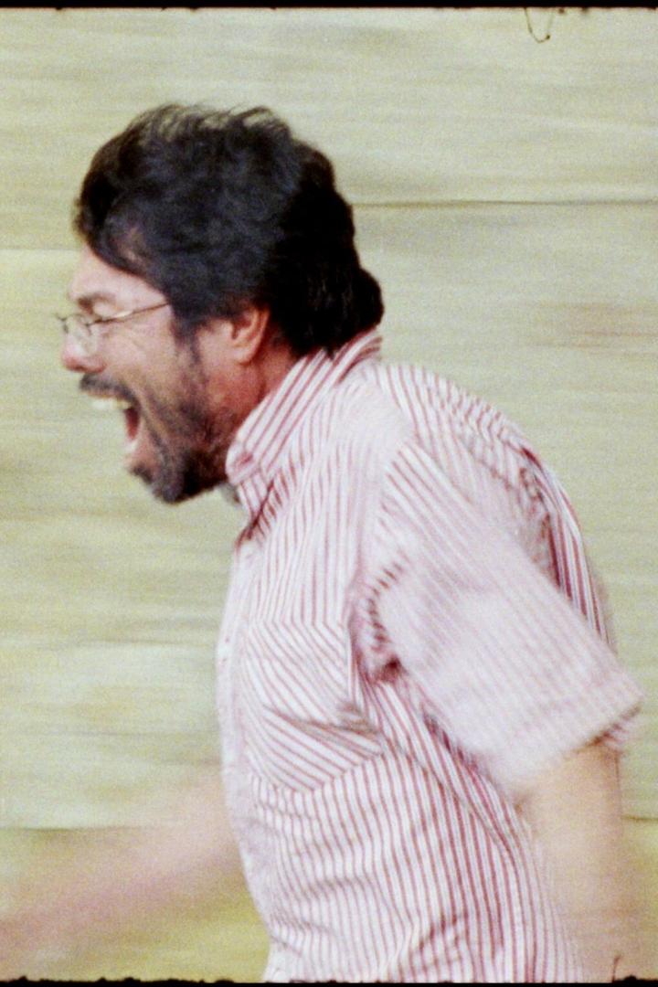 Ein Mann mit Brille und gestreiftem Hemd schreit oder singt.