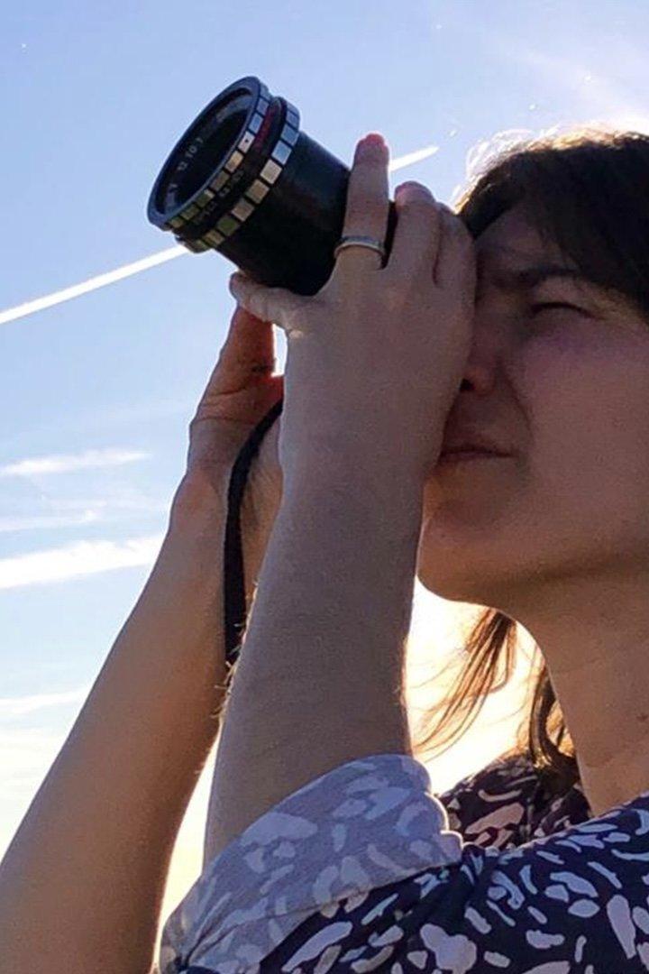 Eine Frau blickt durch ein großes, schwarzes Objektiv in den Himmel.