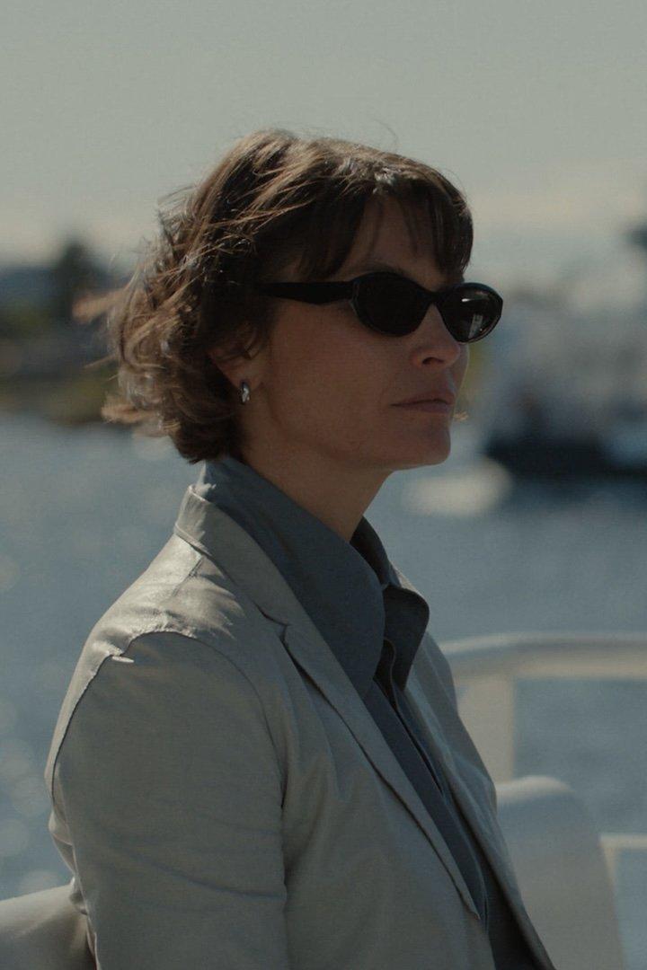 Eine Frau mit Sonnenbrille und Blazer an Bord eines Schiffes.
