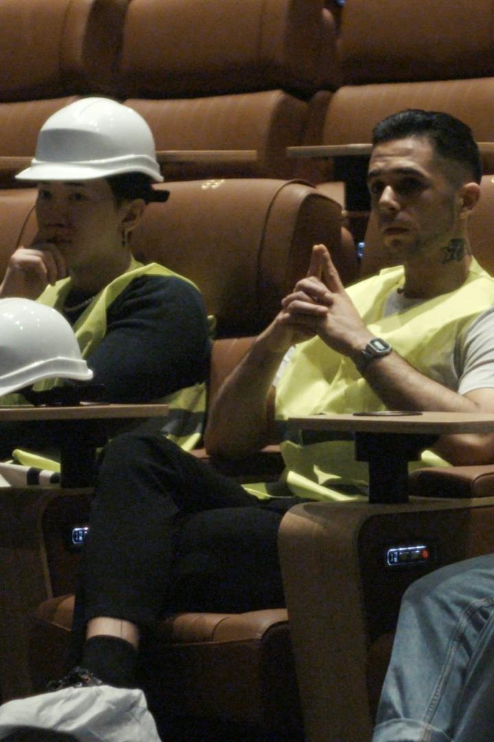 Zwei Bauarbeiter sitzen in einem Kinosaal und machen eine Pause.