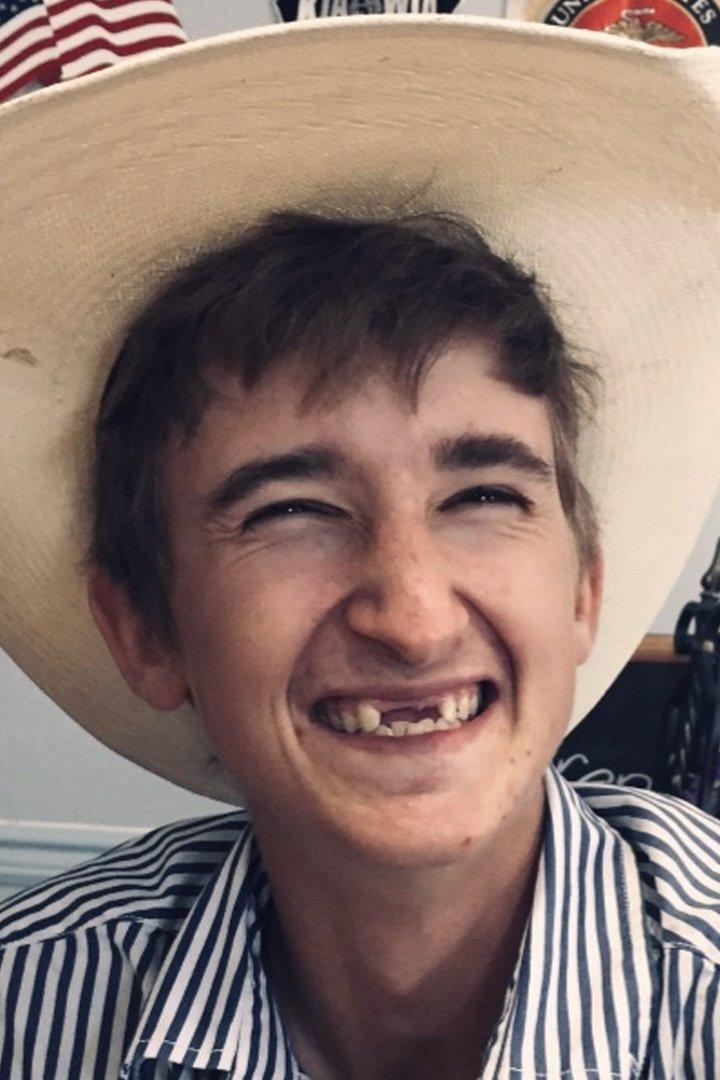 Ein lächelnder junger Mann mit Hut und gestreiftem Hemd.