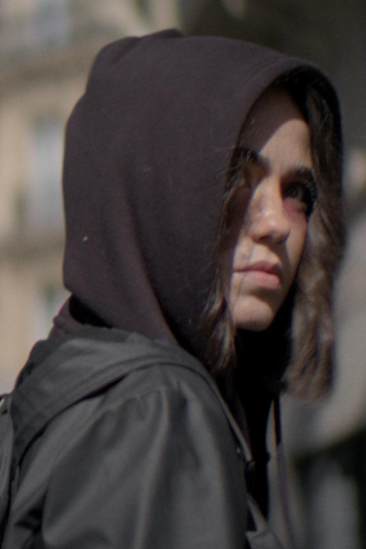 Eine junge Frau mit Kapuze und einem blauen Fleck unter dem Auge blickt in die Ferne.