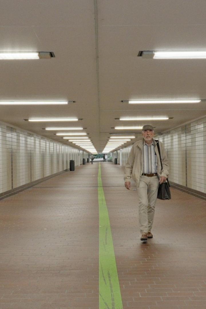 Ein Mann geht in einer Unterführung an einer grünen Linie entlang.