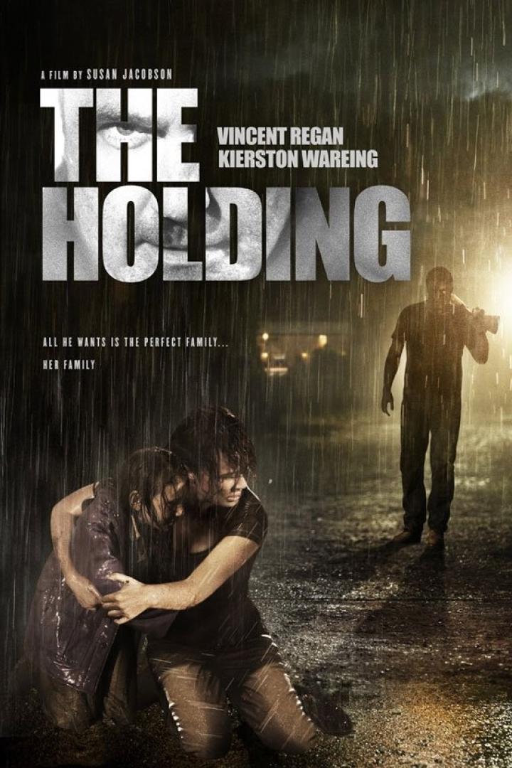 Das Filmplakat für „The Holding“ zeigt ein Paar im Regen und eine bedrohliche Gestalt im Hintergrund.