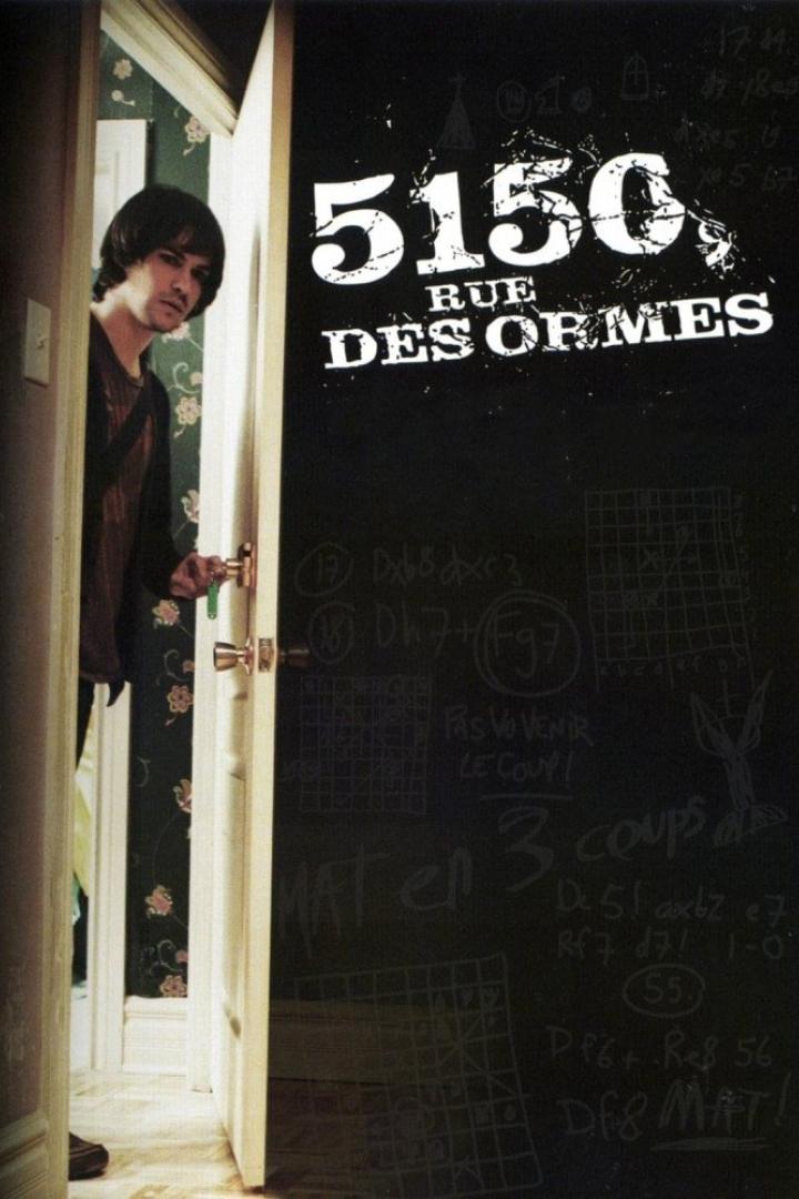 Ein Mann steht in einer Tür; im Hintergrund eine Wand mit der Aufschrift „5150, Rue des Ormes“.