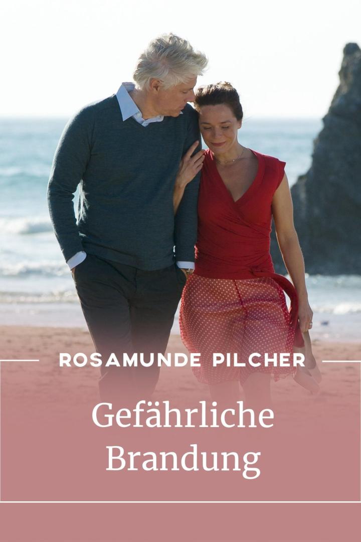 Ein älteres Paar geht am Strand entlang, möglicherweise eine Szene aus „Gefährliche Brandung“ von Rosamunde Pilcher.