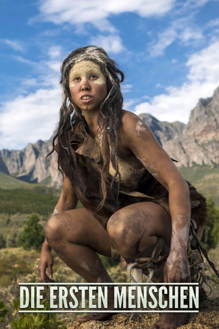Eine junge Frau in Fellkleidung kauert vor einer Bergkulisse.