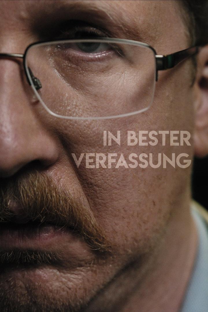 Nahaufnahme eines Mannes mit Brille und Schnurrbart, mit dem Schriftzug „In bester Verfassung“.