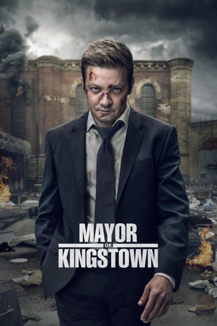Ein verletzter Mann im Anzug steht vor einem Gefängnis im Hintergrund, Titelbild für „Mayor of Kingston“.