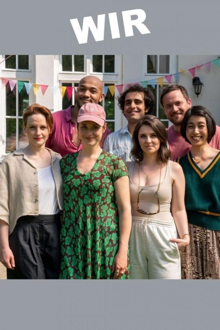 Eine Gruppe von sieben Personen steht vor einem Haus mit bunten Girlanden.