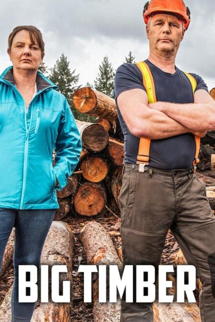 Ein Mann mit Schutzhelm und eine Frau stehen vor einem Stapel Baumstämme für die Sendung „Big Timber“.
