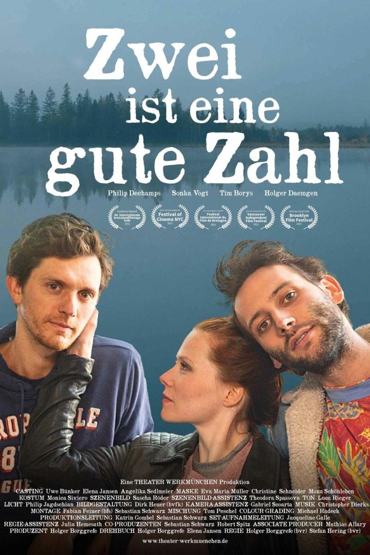 Das Filmplakat zu „Zwei ist eine gute Zahl“ zeigt drei Schauspieler vor einem See.