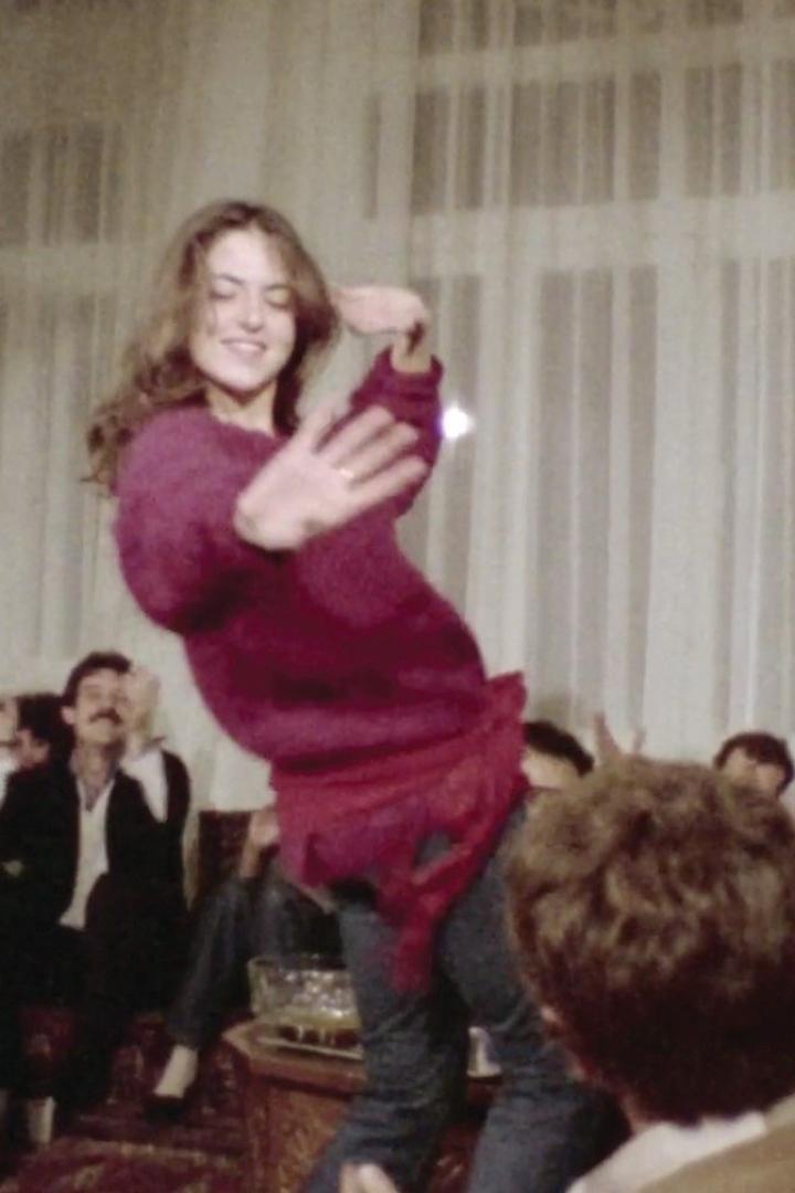 Eine junge Frau tanzt auf einem Tisch, umgeben von Zuschauern.