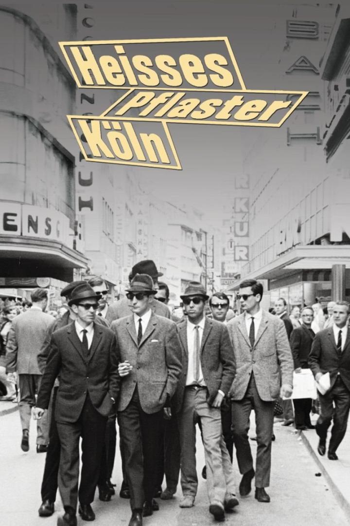 Männer in Anzügen und Hüten gehen in Köln die Straße entlang.