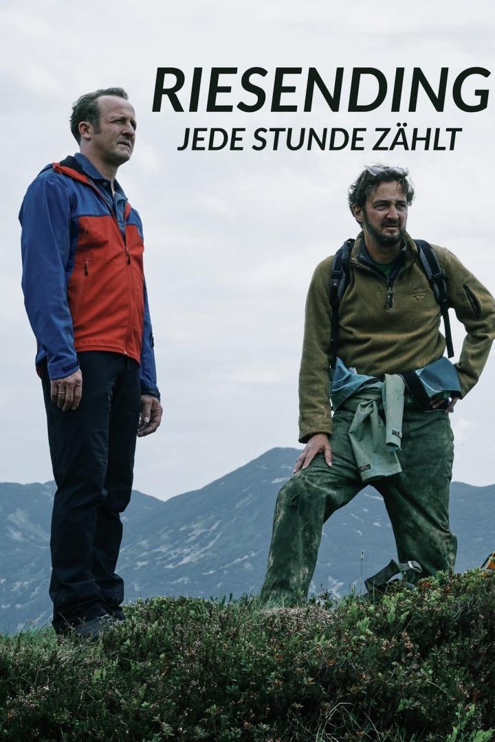 Zwei Männer stehen vor einer Bergkulisse, vermutlich eine Szene aus dem Film „Riesending: Jede Stunde zählt“.