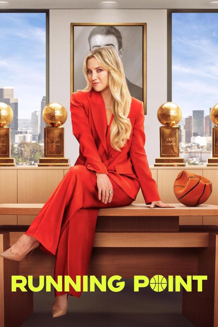 Kate Hudson sitzt in rotem Hosenanzug auf einem Tisch vor Basketballtrophäen und einem Basketball für „Running Point“.