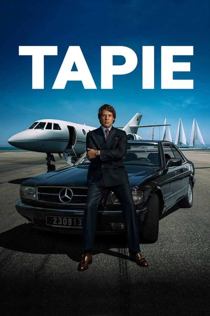 Ein Mann im Anzug posiert vor einem Privatjet, einem Oldtimer-Mercedes und Segelbooten für die Serie „Tapie“.