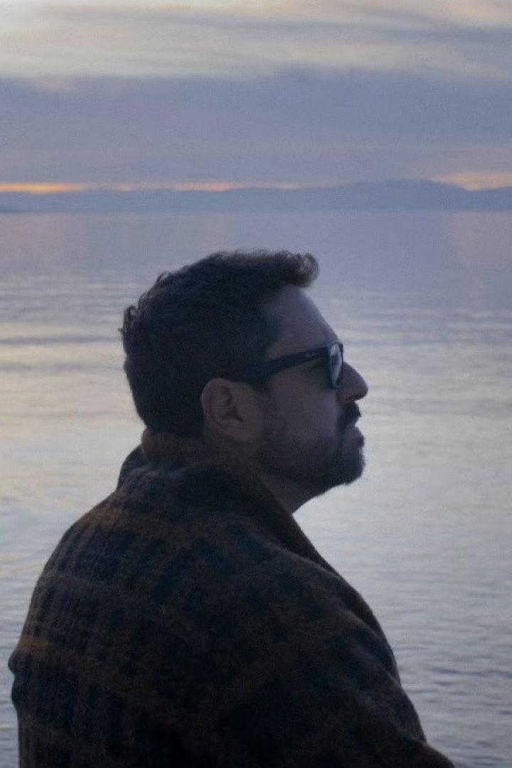 Ein Mann mit Sonnenbrille blickt auf das ruhige Wasser bei Dämmerung.